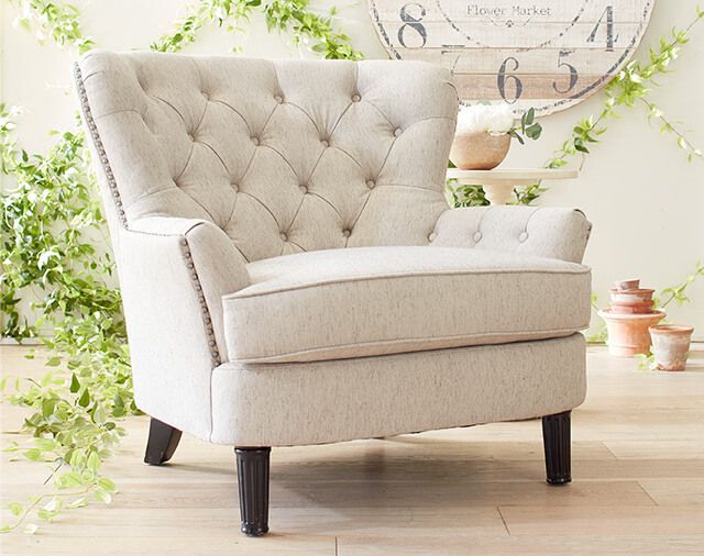 cushioned chair at an angle on wood floor with plants behind and wall decor