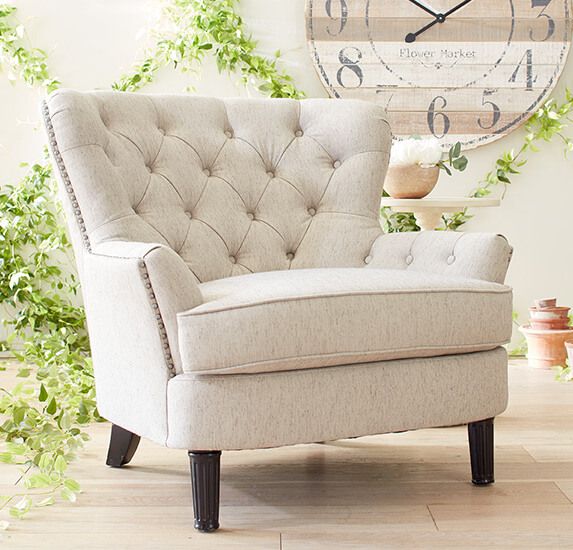 cushioned chair at an angle on wood floor with plants behind and wall decor